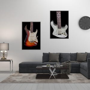 Pu&ograve; includere: Due stampe incorniciate di chitarre elettriche. Una presenta una chitarra con finitura sunburst, l'altra argentata, entrambe su sfondo nero. Sono appese a una parete bianca sopra un divano angolare grigio.