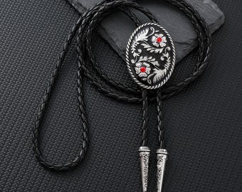 May include: A black leather bolo tie with an oval silver-tone pendant. The pendant features a floral design with red accents. The tie has decorative silver-tone tips.