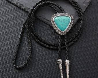 Könnte beinhalten: Schwarze Leder-Bolo-Krawatte mit einem dreieckigen Anhänger aus türkisfarbenem Stein. Der Anhänger ist von einem silberfarbenen Metallrand umgeben. Die Krawatte hat dekorative silberfarbene Metallspitzen und eine geflochtene Lederschnur.