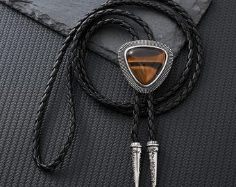 May include: A black braided bolo tie with a silver triangular pendant featuring a brown tiger's eye gemstone.