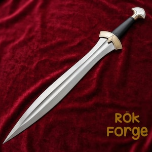 Könnte beinhalten: Ein silbernes Schwert mit einer doppelschneidigen Klinge, einem schwarzen Griff und goldfarbenen Akzenten. Das Schwert wird auf einer roten Samtoberfläche präsentiert. Der Text "Rök Forge" ist in goldfarbenen Buchstaben.