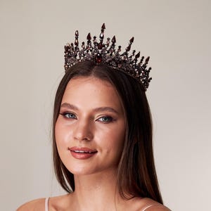 以下が含まれることがあります： 装飾的なディテールと輝くアクセントが施された、濃いバーガンディ色の王冠。王冠は頭に着用されています。王冠は特別な機会に適したフォーマルなアクセサリーです。