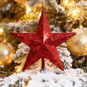Könnte beinhalten: Ein roter, glitzernder Stern als Baumspitze mit einem fünfzackigen Design. Der Stern befindet sich vor einem Hintergrund aus einem Weihnachtsbaum mit schneebedeckten Ästen und goldenen Kugeln. Festliche Weihnachtsdekoration.