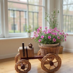 May include: A decorative, handcrafted wicker tractor planter with a basket for flowers. The tractor has four woven wheels and a brown wooden base. The basket is filled with vibrant pink flowers, creating a charming display.