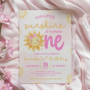 Puede incluir: Invitación de cumpleaños rosa y amarilla con el texto "Our Little Sunshine is Turning One". La invitación presenta un sol sonriente con un lazo rosa. Los detalles incluyen la fecha, la hora y el lugar de la fiesta.