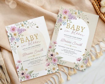 May include: Two baby shower invitations with floral designs. The invitations feature the text "Baby in Bloom" in gold script, along with event details. The invitations are decorated with watercolor flowers in shades of pink, purple, and white.
