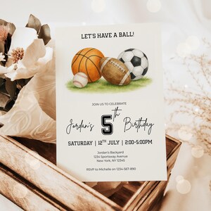 May include: A birthday invitation featuring watercolor illustrations of a basketball, football, baseball, and soccer ball on green grass. The text reads "Let's Have a Ball!" and announces Jordan's 5th birthday on July 12th.