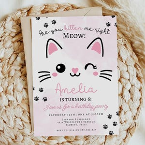 May include: A pink and white birthday invitation featuring a cartoon cat face. The invitation reads "Are you kitten me right MEOW!" and "Amelia is turning 6!" with party details and RSVP information. Black paw prints decorate the edges of the card.