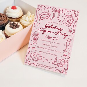 K&ouml;nnte beinhalten: Eine rosa Galentine's Pyjamaparty-Einladung mit Illustrationen einer Schlafmaske, Pyjamas, Hausschuhen und Cocktails. Die Einladung enth&auml;lt Datum, Uhrzeit, Ort und RSVP-Informationen. Cupcakes in einer Box sind im Hintergrund.