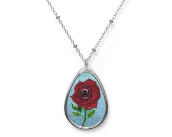 May include: Silver-toned necklace with a pendant featuring a red rose with fangs and a light blue background. The rose has an open mouth with visible fangs. The pendant is oval-shaped and hangs from a delicate chain.