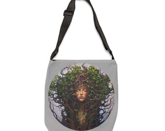 May include: A grey canvas tote bag with a black adjustable shoulder strap. The bag features a circular design of a woman's face surrounded by green leaves and branches.