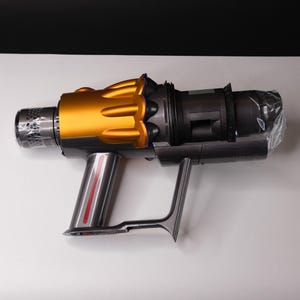 May include: A handheld vacuum cleaner with a gold and gray design. The vacuum has a gold top, a gray body, and a silver handle with a red stripe. The vacuum is on a white surface with a black background.