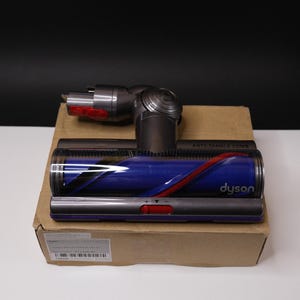 May include: A Dyson vacuum cleaner head and attachment, featuring a blue and red brush roll. The image shows the vacuum components on a cardboard box, with the Dyson logo visible. The anti-tangle comb is also visible.