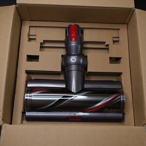 May include: A grey and dark grey vacuum cleaner floor head attachment with a red release button and a rotating brush bar inside a clear housing. The word Dyson is printed on the clear plastic. The attachment is secured in a cardboard box.