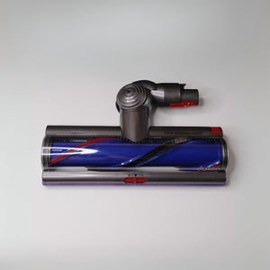May include: A Dyson vacuum cleaner head with a dark gray body, a blue roller brush, and red accents. The head is designed for hair removal and has the Dyson logo on the side.