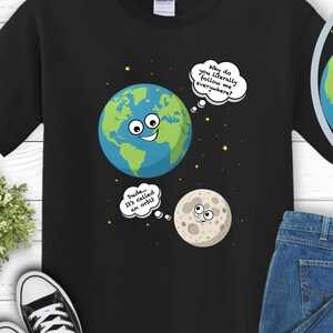 May include: Black t-shirt featuring a cartoon Earth and Moon design with speech bubbles. The Earth and Moon have smiling faces. The shirt is styled with blue jeans and black trainers.