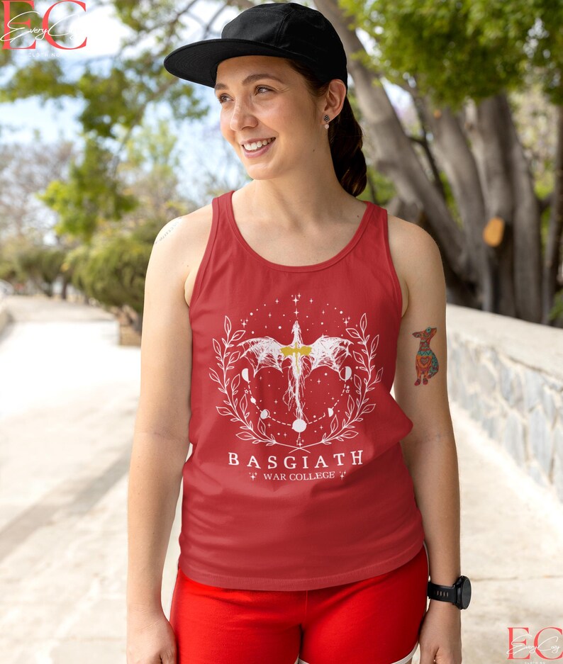 May include: Red vest top with a white graphic design featuring a winged creature, celestial elements, and the text "BASGIATH WAR COLLEGE". The top is worn with a black cap and red shorts.