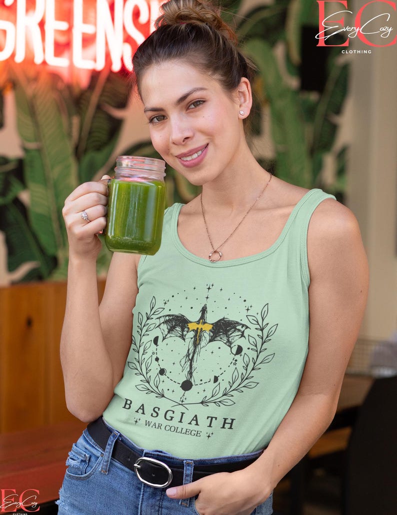 May include: A pale green vest top with a black dragon and moon graphic, and the text "BASGIATH WAR COLLEGE". The top is worn with blue jeans and a black belt. The person is holding a glass jar filled with green liquid.