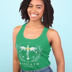 May include: A green vest top with a white graphic design featuring a stylized bird, celestial elements, and the text "BASGIATH WAR COLLEGE". The design is framed by a leafy wreath. The vest top is worn with blue jeans.
