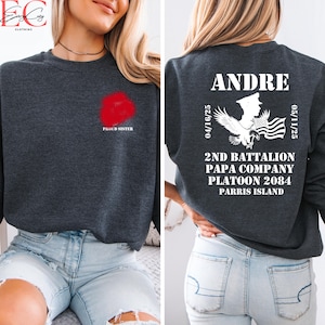 May include: A dark gray sweatshirt with a red floral design and the words "PROUD SISTER" on the front. The back of the sweatshirt features the name "ANDRE", military insignia, and text including "2ND BATTALION" and "PARRIS ISLAND".
