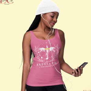 May include: A pink vest top with a white graphic design. The design includes a winged figure, a floral wreath, and the text "BASGIATH WAR COLLEGE". The top is worn with a white beanie hat.