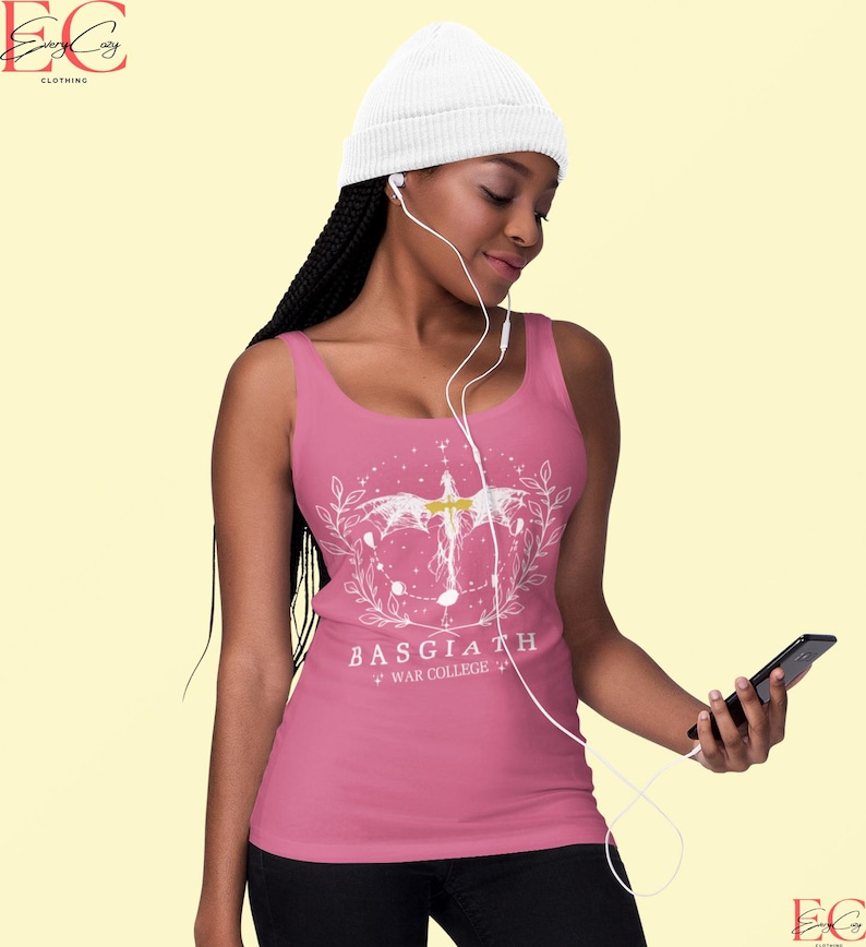 May include: A pink vest top with a white graphic design. The design includes a winged figure, a floral wreath, and the text "BASGIATH WAR COLLEGE". The top is worn with a white beanie hat.