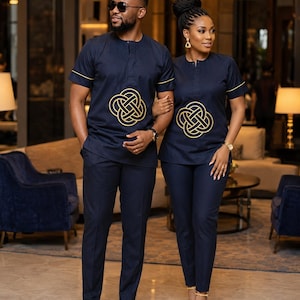 May include: Matching navy blue outfits. The outfits include short-sleeved shirts with gold trim and a gold knot design, paired with matching pants. The man wears black dress shoes, and the woman wears gold heels.