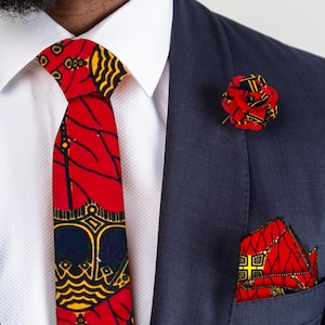 Könnte beinhalten: Ein Set aus Krawatte, Einstecktuch und Reversblume mit rotem, gelbem und marineblauem Muster. Die Krawatte hat ein sich wiederholendes Muster. Das Einstecktuch ist gefaltet und in einer marineblauen Anzugtasche platziert. Die Reversblume ist rot und gelb.