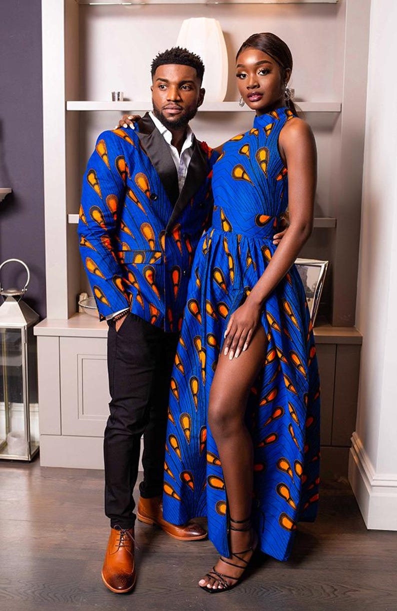 May include: A blue blazer with black lapels and a blue sleeveless high-neck dress, both featuring a vibrant orange and yellow teardrop pattern. The dress includes a floor-length skirt with a high side slit, while the blazer is paired with black trousers.