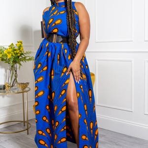 May include: A sleeveless maxi dress in a vibrant blue fabric featuring a repeating orange and black teardrop pattern. The dress has a high neckline, a fitted waist accented by a wide black belt with a gold buckle, and a high front leg slit.