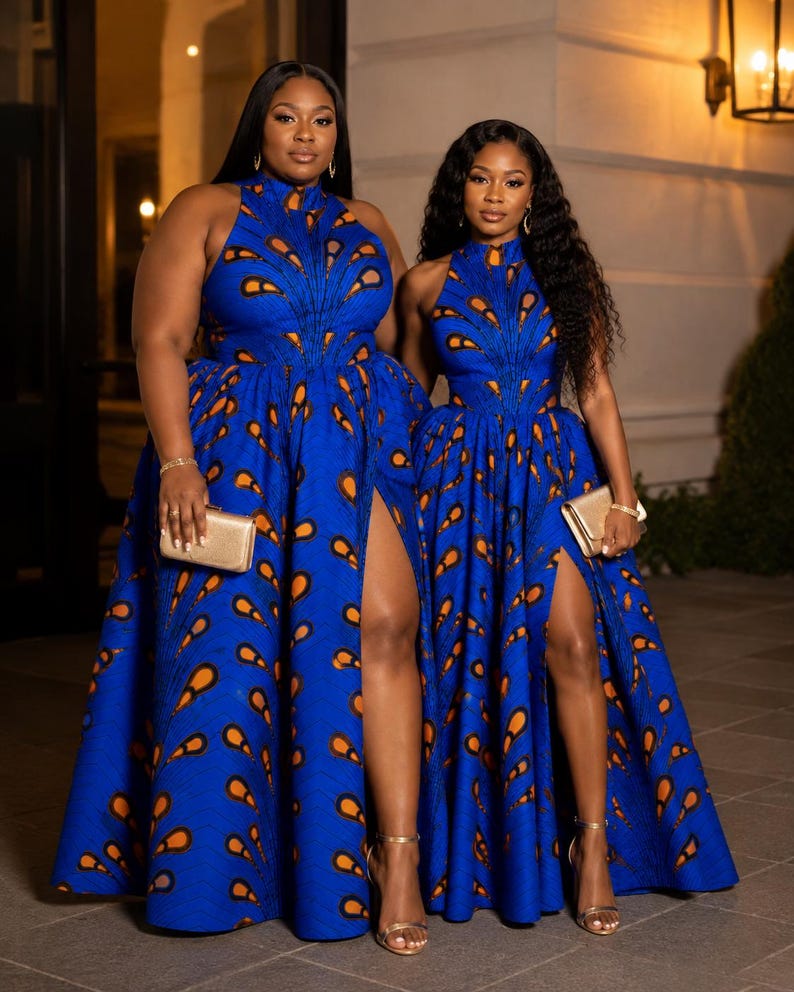 May include: Two floor-length blue dresses featuring a high neckline and a repeating orange and black teardrop pattern. Each dress has a fitted bodice, a full skirt with a high side slit, and is paired with a small gold clutch and gold sandals.