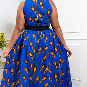 May include: A sleeveless maxi dress in a vibrant blue fabric featuring a repeating orange and black teardrop pattern. The dress has a high neckline, a solid black waistband, and a long, full skirt with a visible gold-toned zipper down the back.