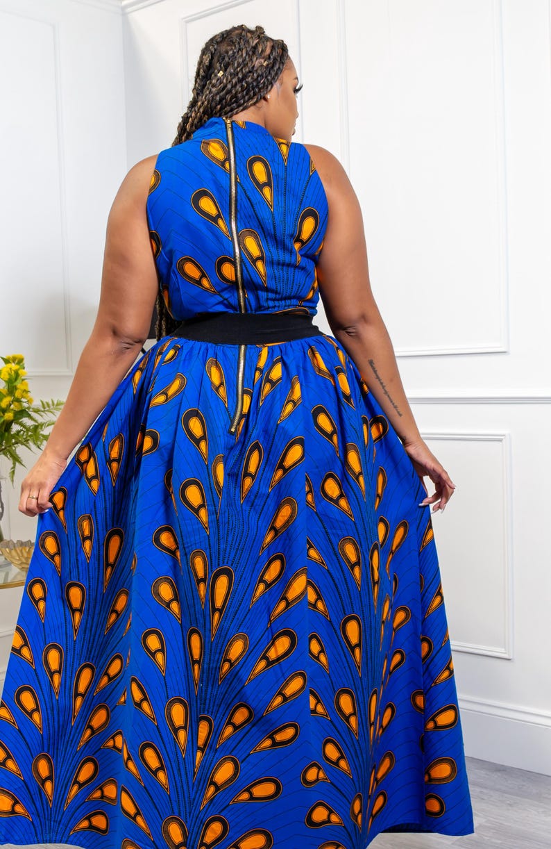 May include: A sleeveless maxi dress in a vibrant blue fabric featuring a repeating orange and black teardrop pattern. The dress has a high neckline, a solid black waistband, and a long, full skirt with a visible gold-toned zipper down the back.