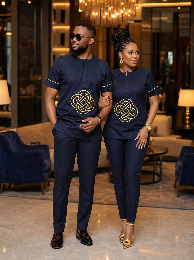 May include: Matching navy blue outfits. The outfits include short-sleeved shirts with gold trim and a gold knot design, paired with matching pants. The man wears black dress shoes, and the woman wears gold heels.