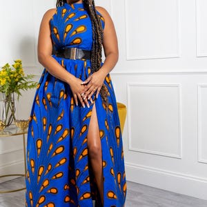May include: A sleeveless floor-length dress in vibrant blue featuring a repeating orange and black teardrop pattern. The garment has a high neckline, a fitted waist accented by a wide black belt with a gold buckle, and a high side slit.
