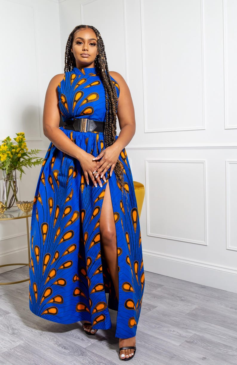 May include: A sleeveless floor-length dress in vibrant blue featuring a repeating orange and black teardrop pattern. The garment has a high neckline, a fitted waist accented by a wide black belt with a gold buckle, and a high side slit.