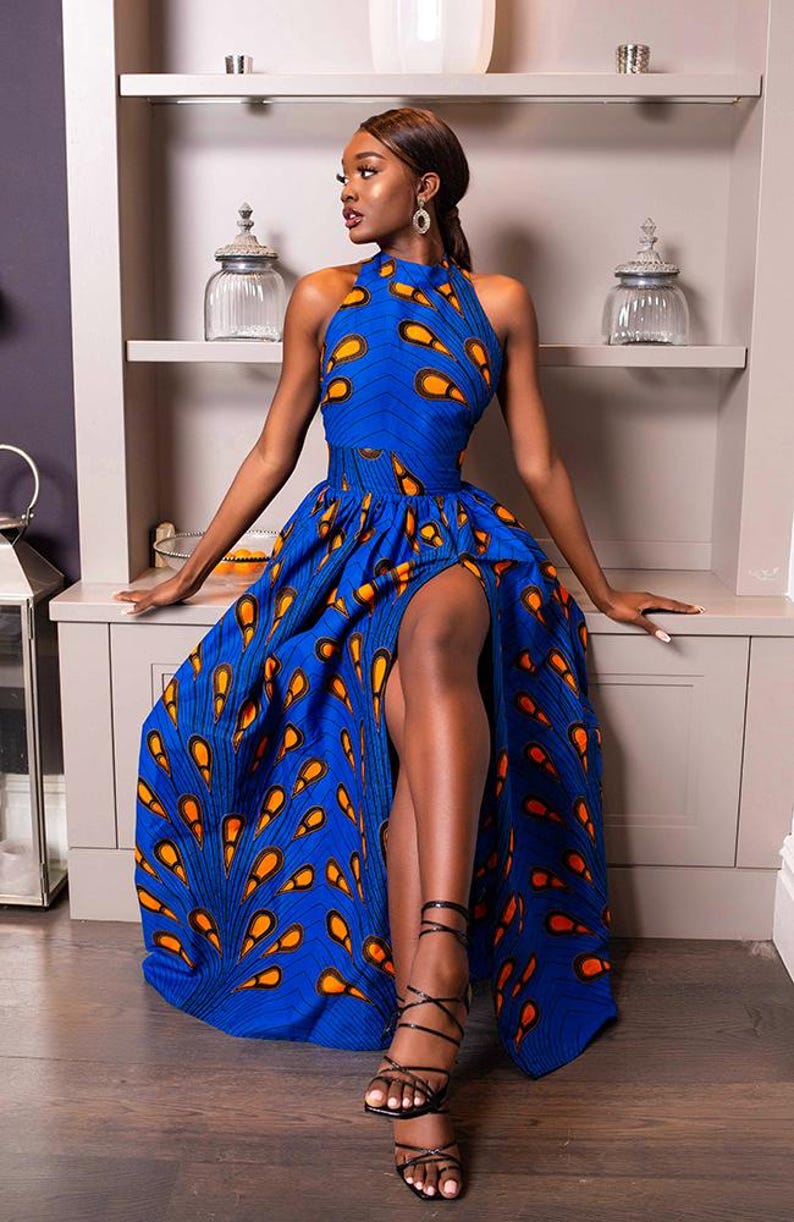 May include: A sleeveless floor-length dress in a vibrant blue fabric featuring a repeating orange and black teardrop pattern. The garment has a high halter neckline, a fitted waist, and a full skirt with a high side slit, paired with black strappy heels.