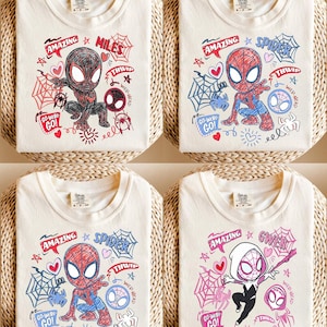 Peut inclure: Quatre t-shirts pliés de couleur crème avec différents motifs de personnages de Spider-Man. Chaque chemise présente un personnage de Spider-Man de dessin animé, des toiles d'araignées, des cœurs et les mots "AMAZING", "GO-WEBS GO!" et "THWIP".