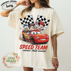 Op de afbeelding: Ivoor kleurig T-shirt met een afbeelding van Disney-figuren in een rode raceauto met geblokte vlaggen. De tekst "SPEED TEAM 1928" staat onder de auto. Het shirt heeft de woorden "COMFORT COLORS" en "Ivory" linksboven.