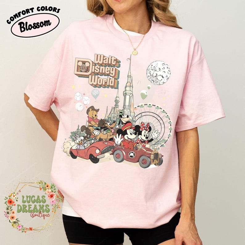 May include: Pink Comfort Colors t-shirt featuring a vintage-style Walt Disney World graphic. The design includes Mickey and Minnie Mouse, Winnie the Pooh, and other characters in classic cars, with the text "Walt Disney World".