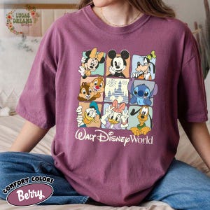 K&ouml;nnte beinhalten: Beerenfarbenes Comfort Colors T-Shirt mit einem Raster von Disney-Figuren, darunter Mickey Mouse, Minnie Mouse, Donald Duck und Stitch. Die Worte "Walt Disney World" sind darunter gedruckt.