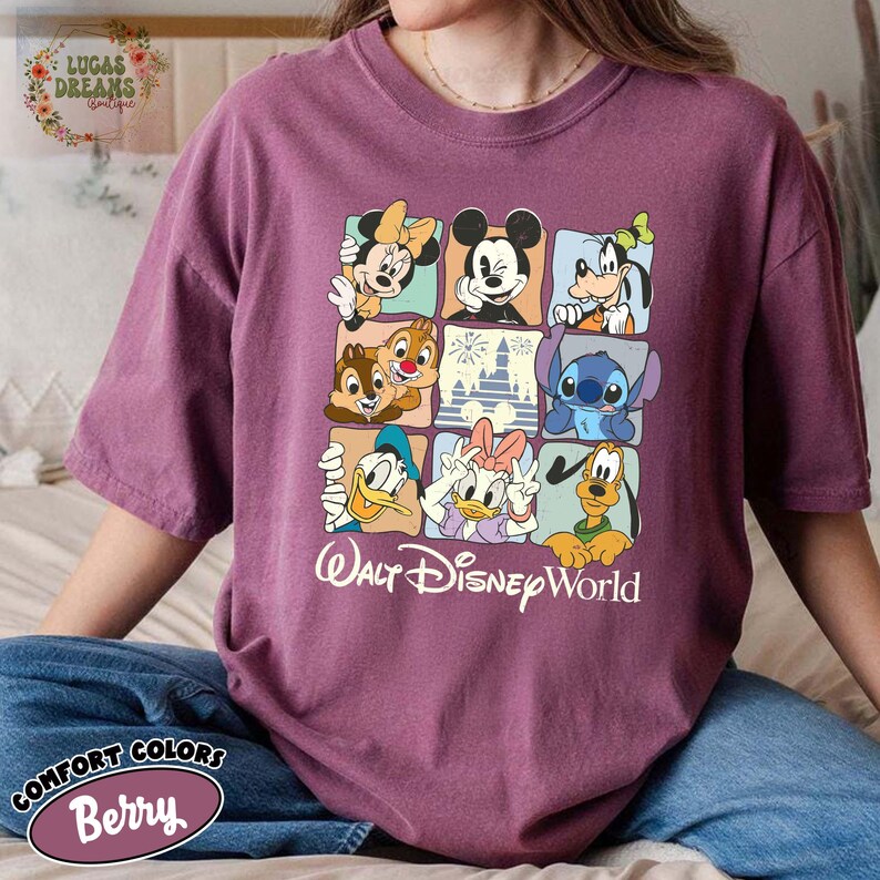 K&ouml;nnte beinhalten: Beerenfarbenes Comfort Colors T-Shirt mit einem Raster von Disney-Figuren, darunter Mickey Mouse, Minnie Mouse, Donald Duck und Stitch. Die Worte "Walt Disney World" sind darunter gedruckt.