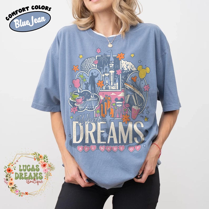 K&ouml;nnte beinhalten: Hellblaues kurz&auml;rmeliges T-Shirt mit einem Grafikdesign mit Themenpark-Symbolen, Blumen und dem Text "What Dreams Are Made Of". Das T-Shirt hat einen Rundhalsausschnitt und die Worte "Comfort Colors Blue Jean" sind oben links aufgedruckt.