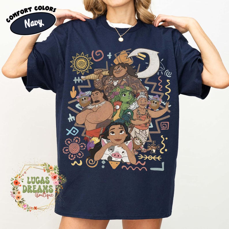 May include: A navy blue short-sleeve t-shirt featuring a graphic print of characters from the movie Moana, including Moana, Maui, Pua, Hei Hei, and Gramma Tala, surrounded by colorful tribal-inspired patterns and symbols on the front.