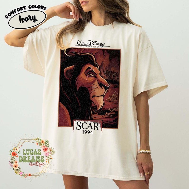 May include: An ivory-colored t-shirt featuring a graphic print of the character Scar from the 1994 Walt Disney film. The design includes the text Walt Disney Pictures Presents, Scar, and 1994, showcasing the lion in a dark, cave-like setting.