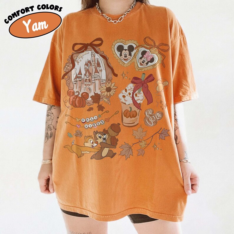 May include: Orange t-shirt with a graphic featuring a castle, Mickey and Minnie Mouse, Chip and Dale, and fall-themed elements. The shirt has the text "Comfort Colors" and "Yam" in an oval. The design includes pumpkins, acorns, and leaves.