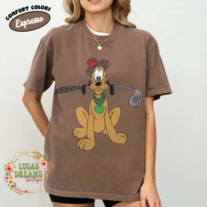 May include: Brown t-shirt featuring a cartoon dog wearing a golf hat and holding a golf club. The shirt has the text "COMFORT COLORS Espresso" at the top and the "LUCAS DREAMS Boutique" logo at the bottom.