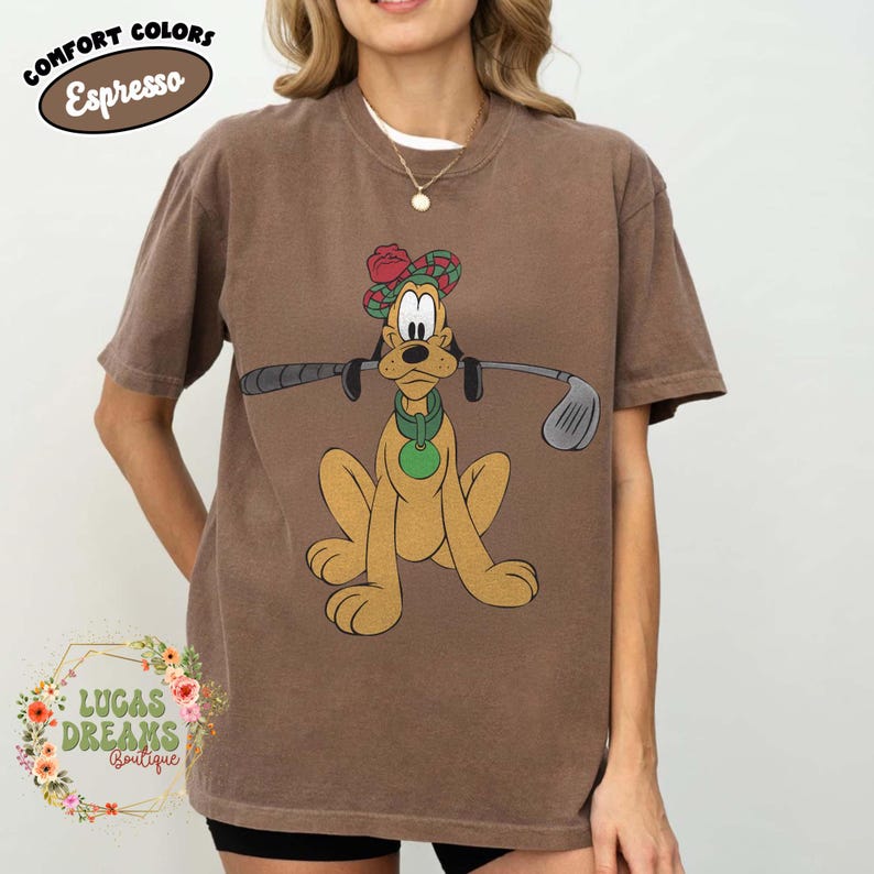 May include: Brown t-shirt featuring a cartoon dog wearing a golf hat and holding a golf club. The shirt has the text "COMFORT COLORS Espresso" at the top and the "LUCAS DREAMS Boutique" logo at the bottom.
