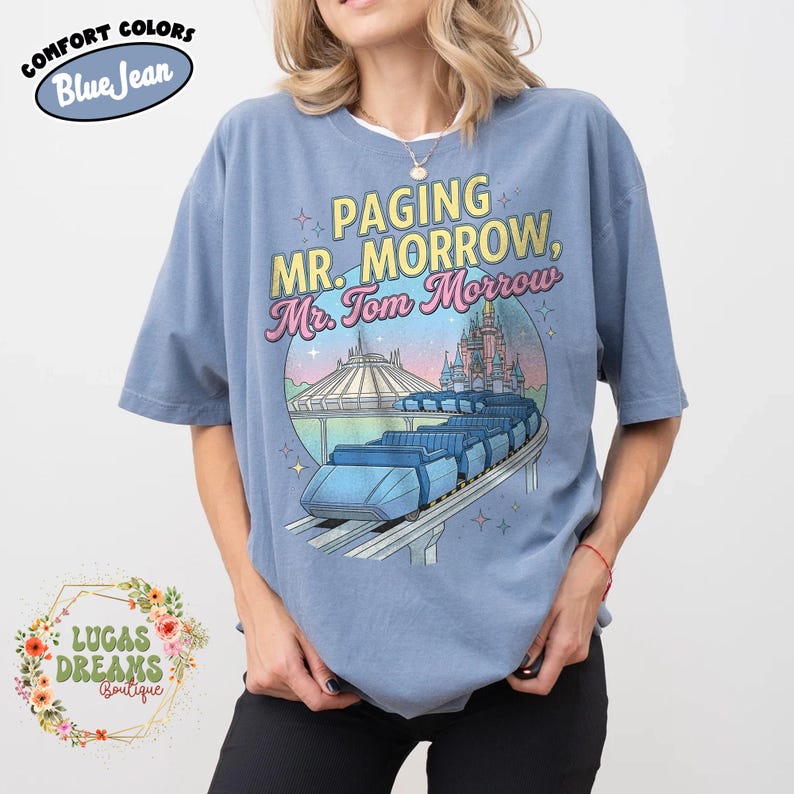 May include: Pale blue t-shirt featuring the text "Paging Mr. Morrow, Mr. Tom Morrow" and a graphic of a futuristic train, Space Mountain, and a castle. The shirt is a comfort colour and has the words "Comfort Colors" and "Blue Jean" on it.