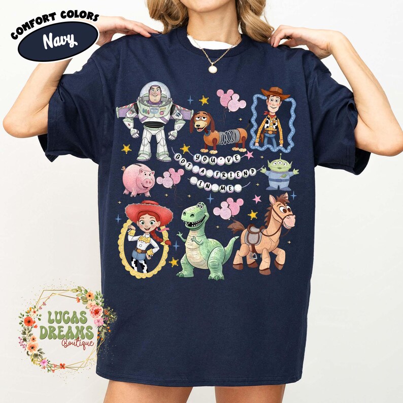May include: Navy blue t-shirt featuring a colorful graphic of Toy Story characters, including Buzz Lightyear, Woody, and Jessie. The text "You've Got a Friend in Me" is also displayed. The shirt has a crew neck and short sleeves.